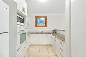 Eine Küche mit weißen Schränken, einer Mikrowelle, einem Backofen, einem Spülbecken und einem gerahmten Bild an der Wand.
