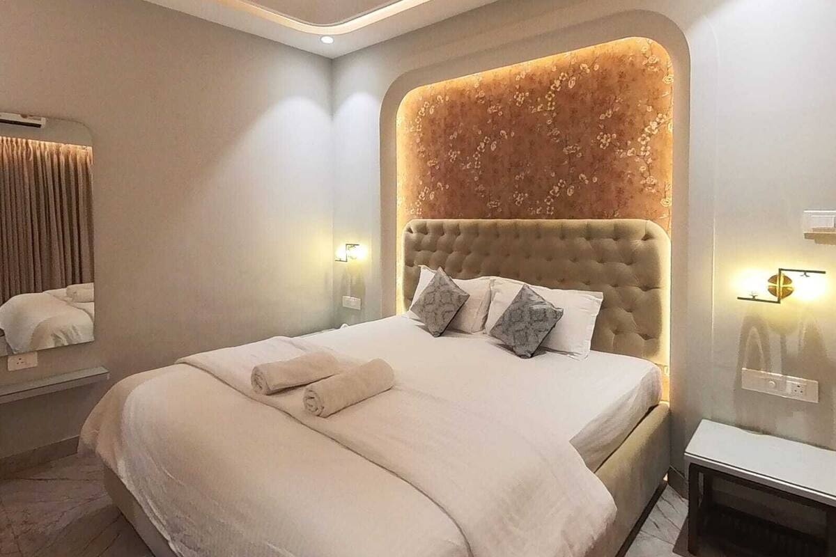 A modern hotel room with a large bed, a tufted headboard, and a mirror on the wall.