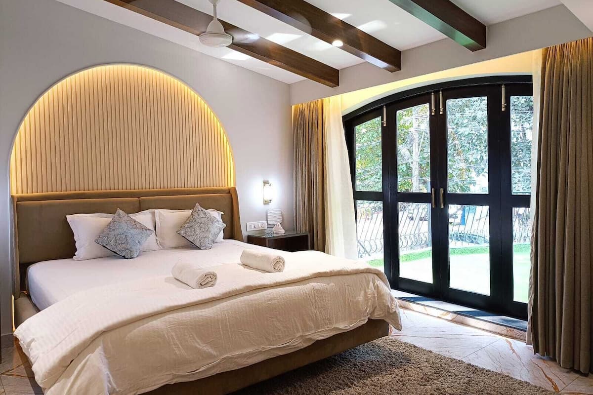 A spacious bedroom with a large bed, a curved wall design, a ceiling fan, and a view through a large window.