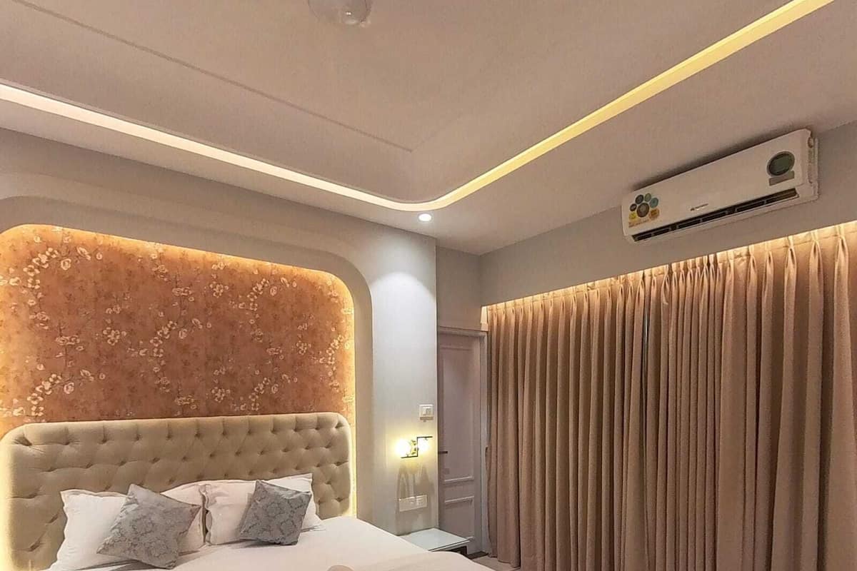 A modern hotel room with a tufted headboard, a large bed with white linens, a rolled towel, and a wall-mounted air conditioning unit.