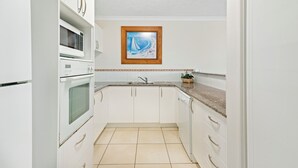 A kitchen with white cabinets, a microwave, an oven, a sink, and a framed picture on the wall.