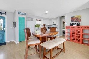 Une cuisine moderne avec des meubles blancs, une table à manger en bois et quatre chaises, ainsi qu’une étagère décorative rouge.