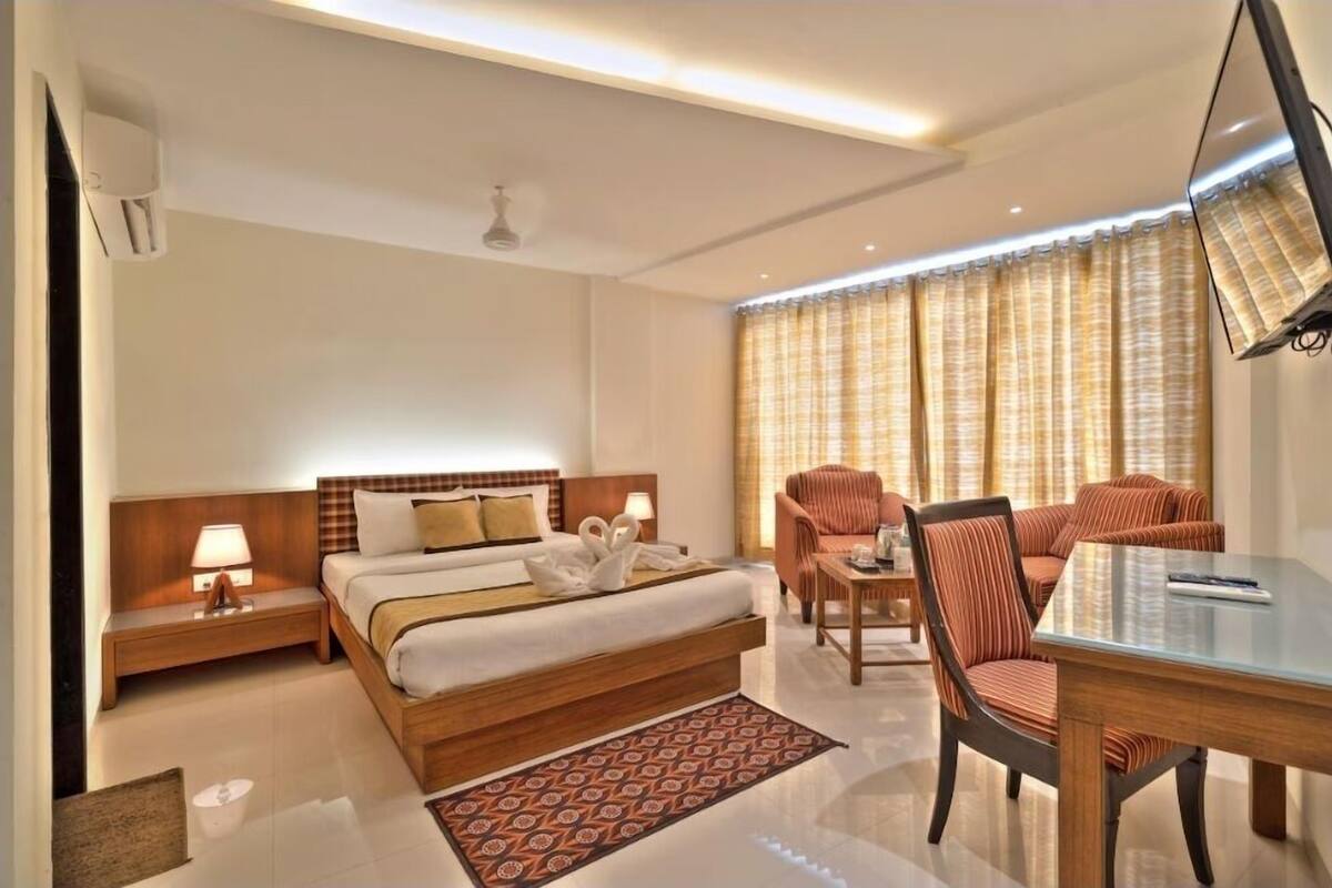 A hotel room with a large bed, a sitting area with a sofa and chairs, a small table, and a TV.