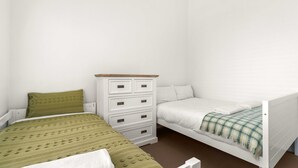 A bedroom with two beds, a white dresser, and a green and white checkered blanket.