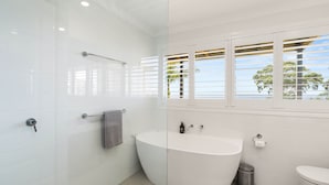 A modern bathroom with a freestanding bathtub, a toilet, and a window with blinds.