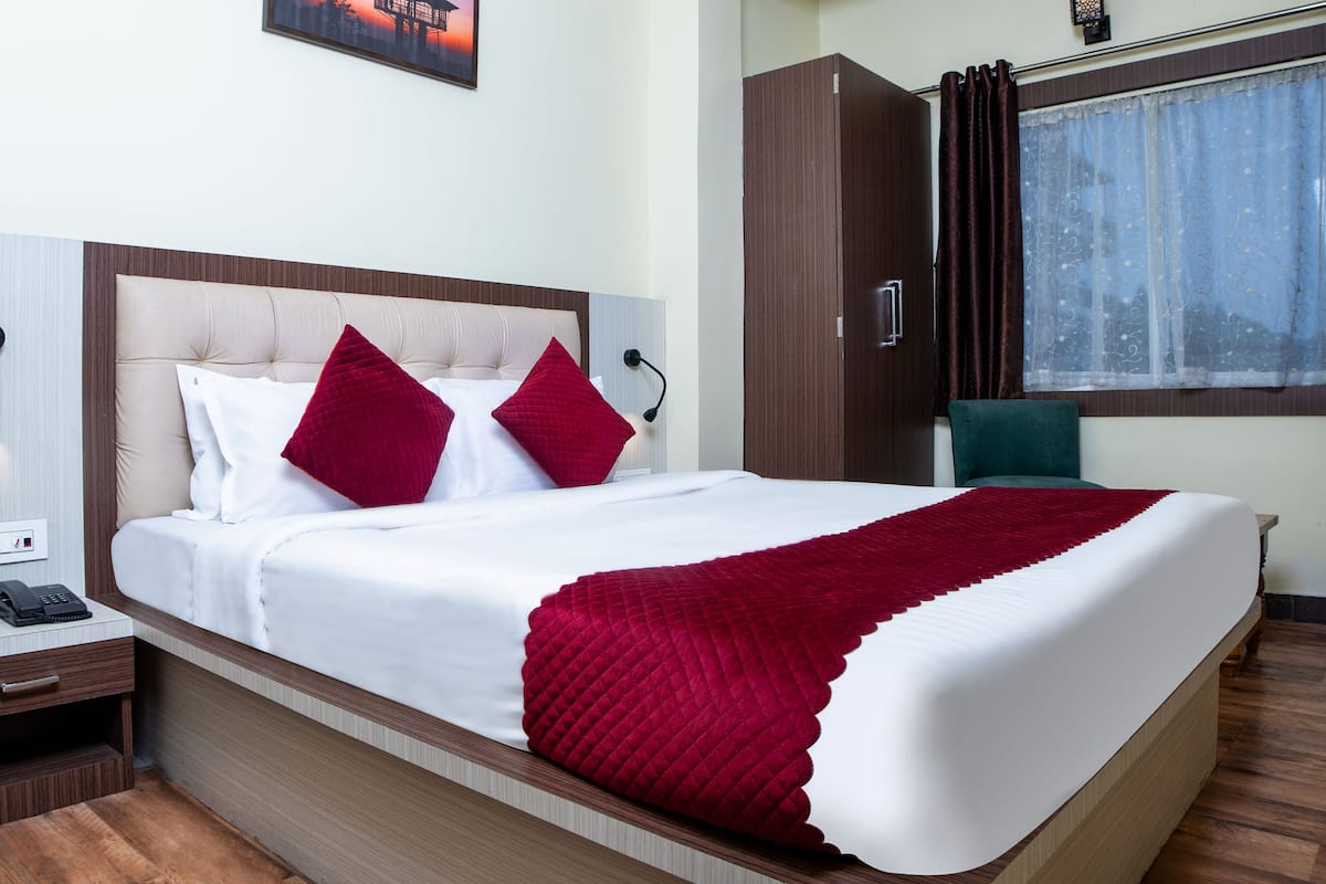A neatly made bed with a white and red quilt, a bedside table with a phone, and a window with curtains.