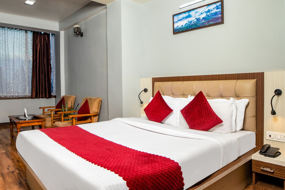 A hotel room with a large bed, two chairs, a small table, a lamp, and a painting on the wall.