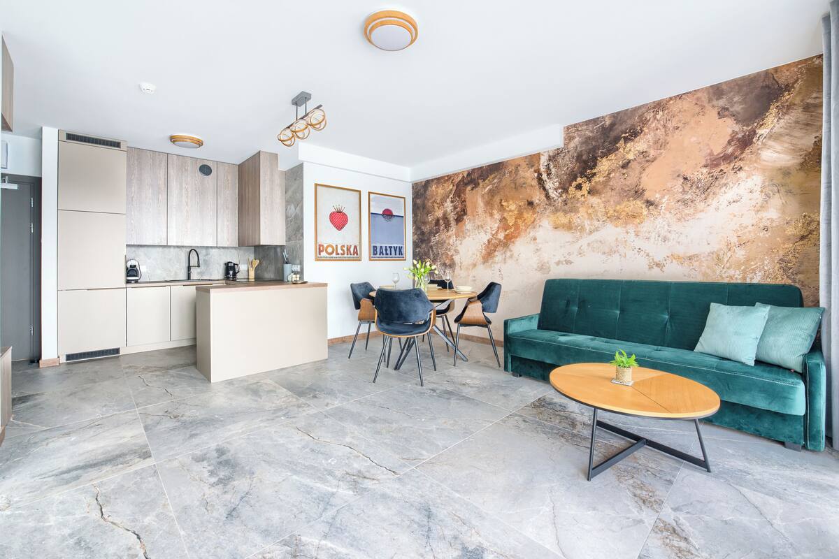 Una cocina moderna con una isla central, un comedor con sofá verde y un gran mural abstracto en la pared.