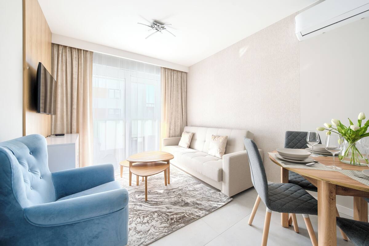 Un salón moderno con un sillón azul, un sofá blanco y una mesa de comedor dispuesta con platos y vasos.
