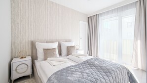 A modern hotel room with a large bed, a bedside table with a round mirror, and a view of the outdoors through sheer curtains. - Apartamenty Sun & Snow Perłowa Przystań Kołobrzeg (Kolobrzeg)