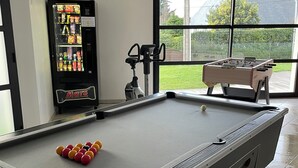 Et billardbord med kugler, et fodboldbord og en automat i et rum med store vinduer.