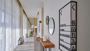 A hotel corridor with a wooden bench, mirrors, and a directional sign indicating amenities like toilets, clinic, restaurant, pool, and promenade.
