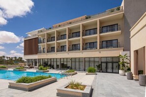 Un hotel de varios pisos con piscina, asientos al aire libre y un jardín bien cuidado.