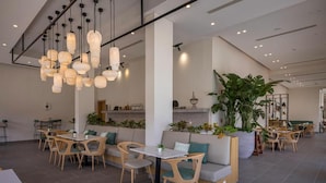 A modern cafe with multiple seating areas, including tables and benches, and a variety of hanging light fixtures.