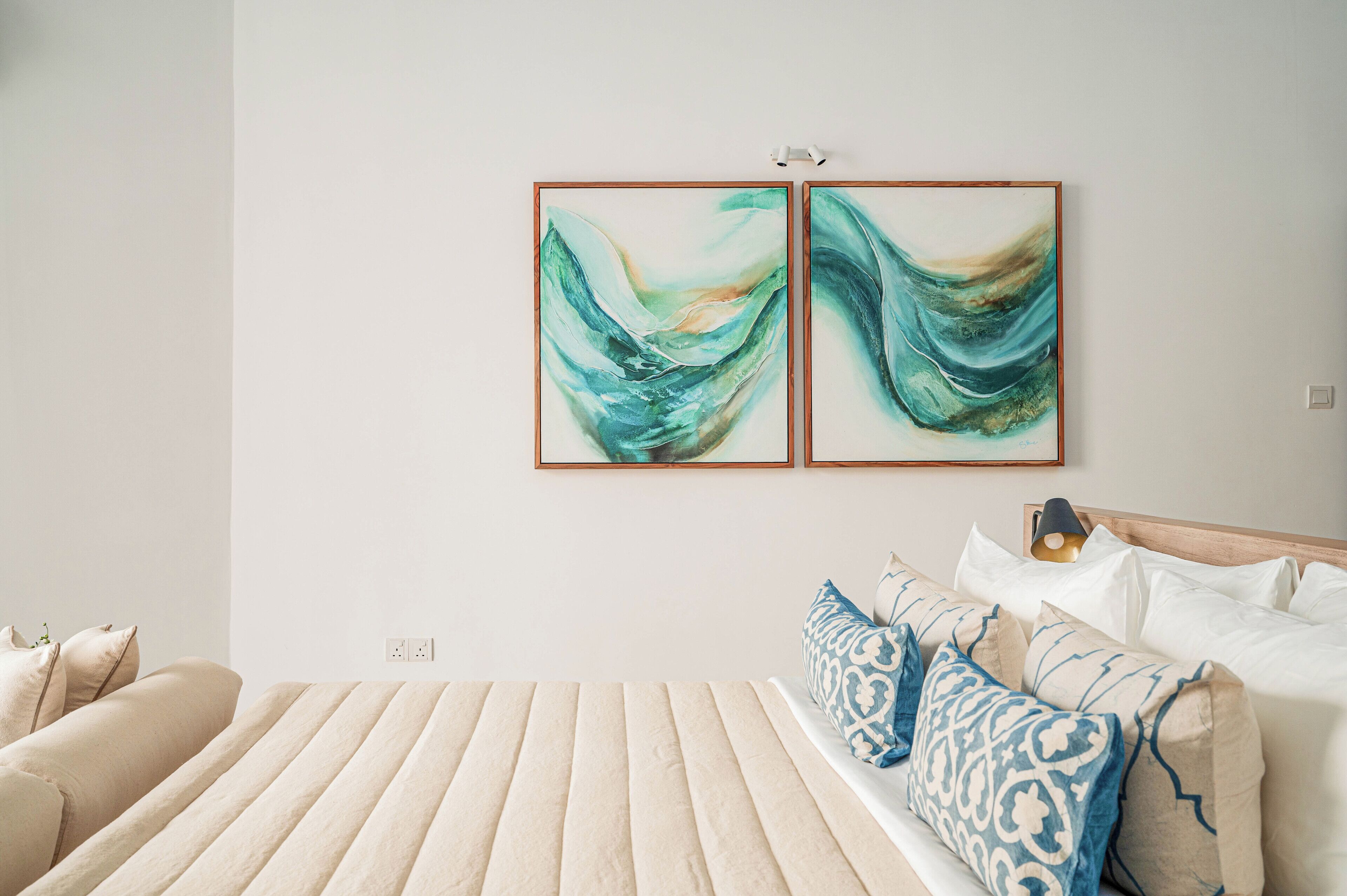 A bedroom with a bed, pillows, and two abstract paintings on the wall.