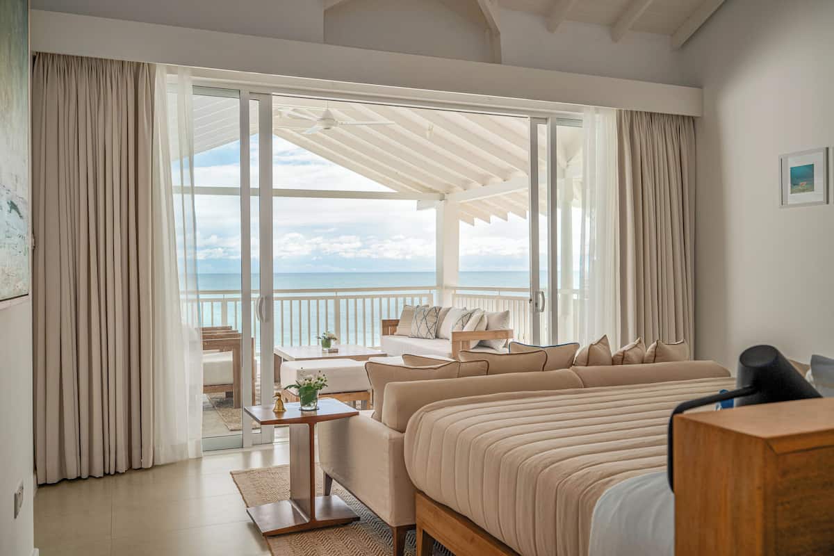 A bedroom with a large bed, a desk, and a view of the ocean through a sliding glass door.