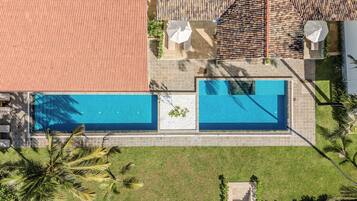Two rectangular pools are surrounded by a lawn and palm trees, bordered by light-colored tiles.