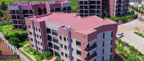 A multi-story residential building with a flat roof, multiple balconies, and a parking area.