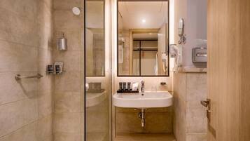 Un baño moderno con cabina de ducha de vidrio, lavamanos con mueble y un espejo.
