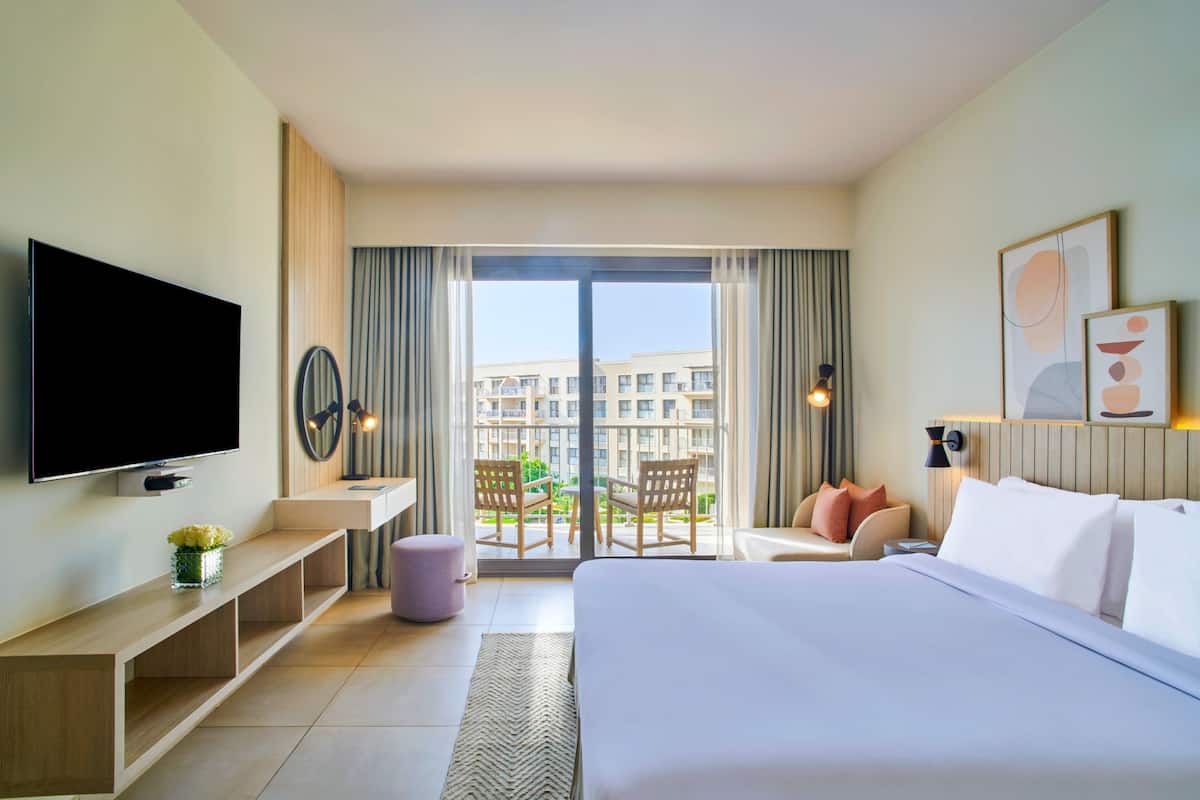 Une chambre d’hôtel avec un grand lit, une télévision, un bureau et un balcon équipé de chaises.