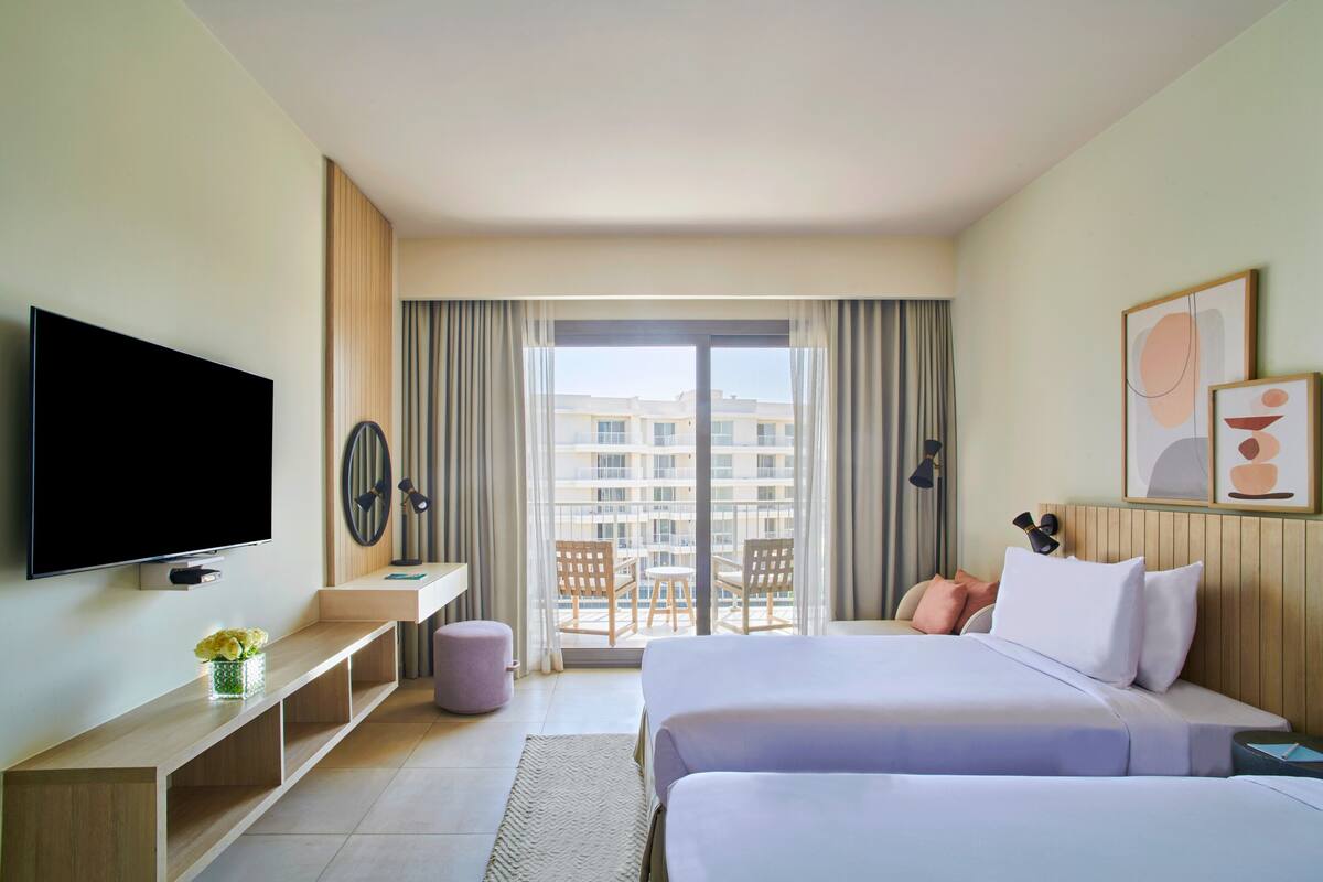 Une chambre d’hôtel avec un lit, une télévision, un bureau et un balcon équipé de chaises.