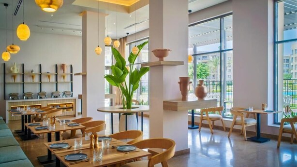 Un restaurant moderne avec des tables et des chaises en bois, de grandes fenêtres et des lampes suspendues.