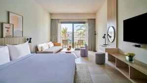 Une chambre d’hôtel équipée d’un lit, d’un canapé, d’une télévision et d’un balcon offrant une vue sur les palmiers.