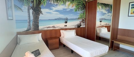 Habitación de hotel con dos camas individuales, una mesita de noche de madera, una pequeña mesa y un mural grande con motivos playeros en la pared.