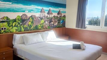 Ein Hotelzimmer mit einem Bett, einem Nachttisch aus Holz und einer Wandmalerei, die eine Strandansicht zeigt.