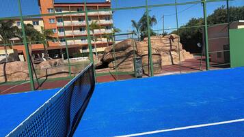 Una cancha de tenis con red, rodeada por una cerca verde.