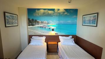 Ein Hotelzimmer mit zwei Einzelbetten, einem Holznachttisch und einem großen Wandbild mit Strandmotiv.
