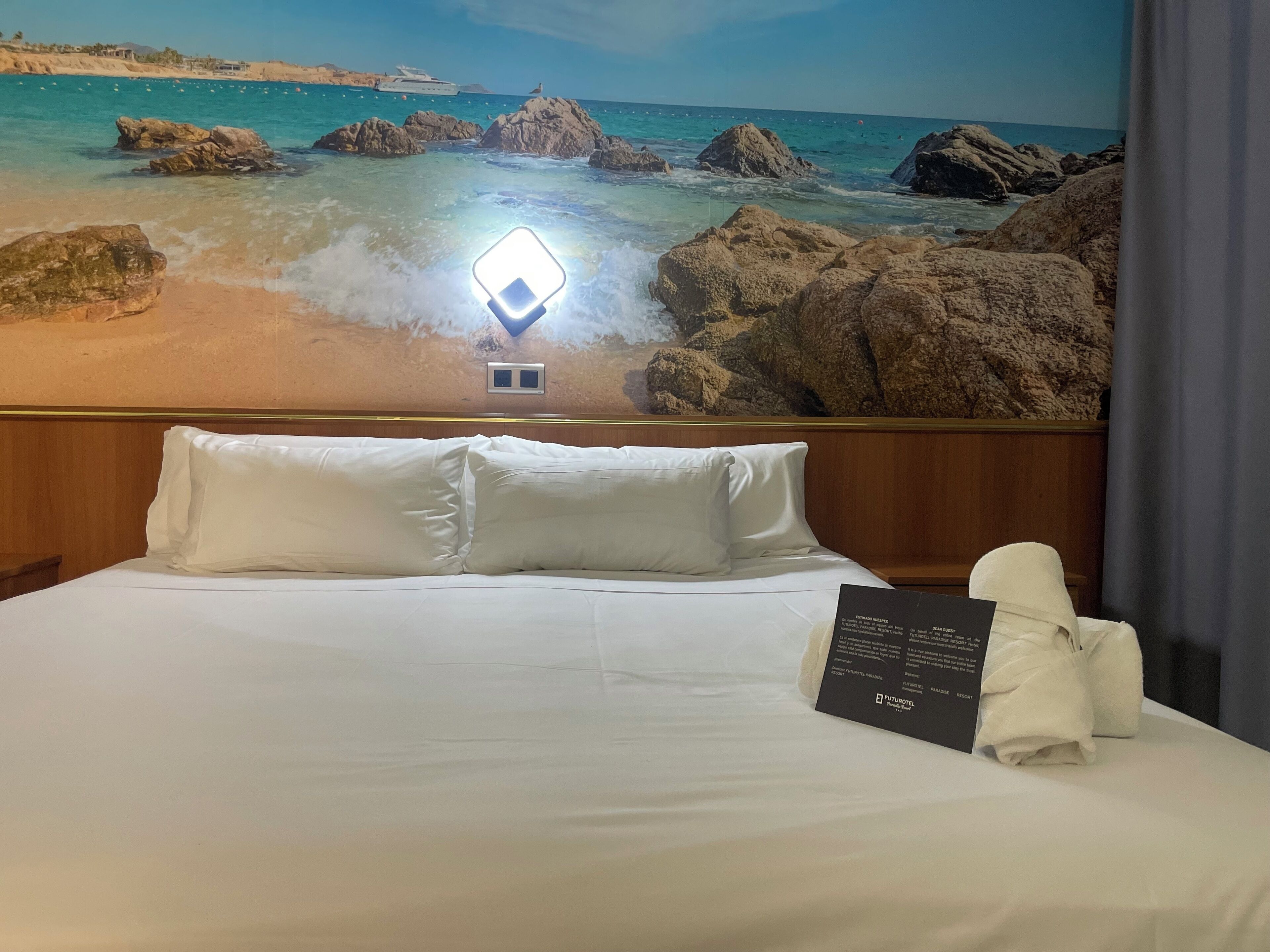 Ein Hotelzimmer mit einem Bett, weißen Kissen, ordentlich bezogenem Bett, einem Handtuch und einem Schild.