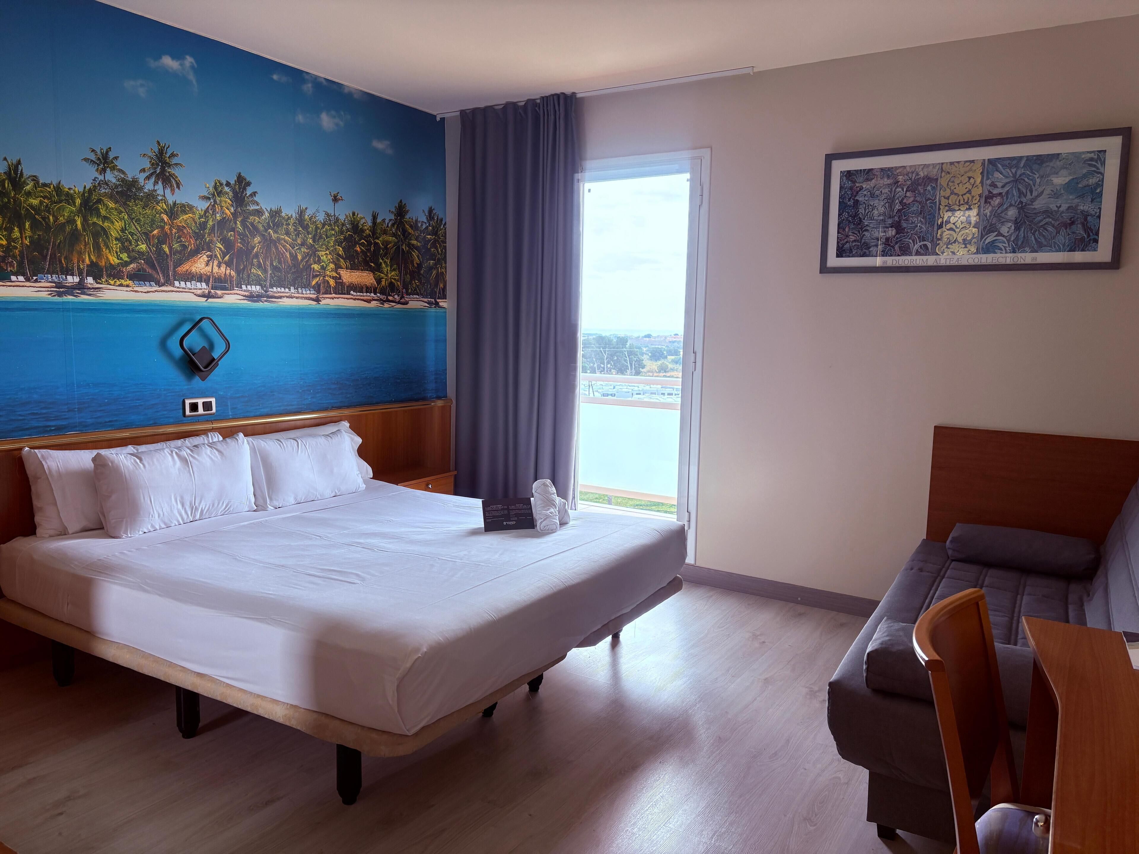 Ein Hotelzimmer mit einem großen Bett, einer Couch, einem Gemälde und Blick auf das Meer.