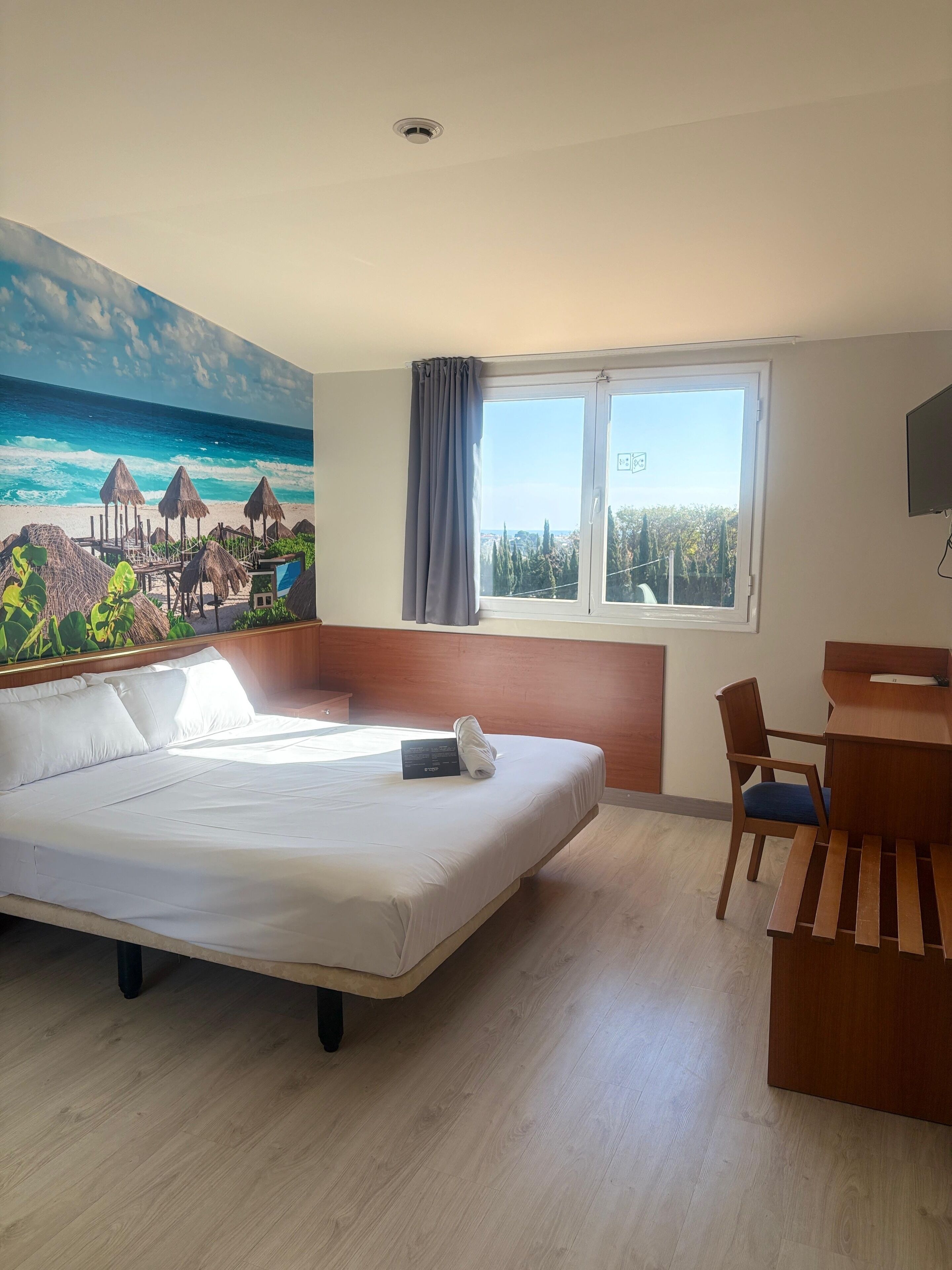 Une chambre d’hôtel avec un lit, un bureau et une vue sur l’océan par la fenêtre.