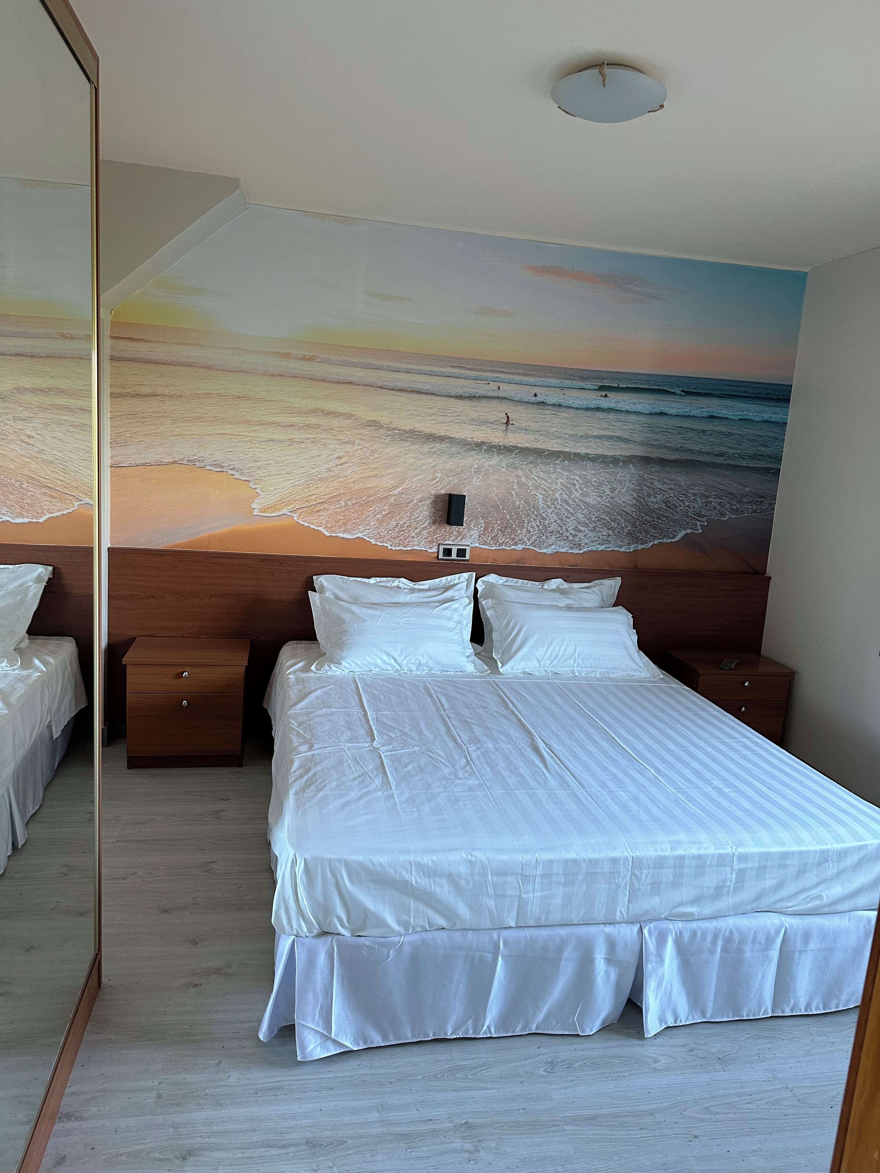 Un dormitorio con una cama grande, dos mesitas de noche, un cabecero de madera y un mural de playa en la pared.
