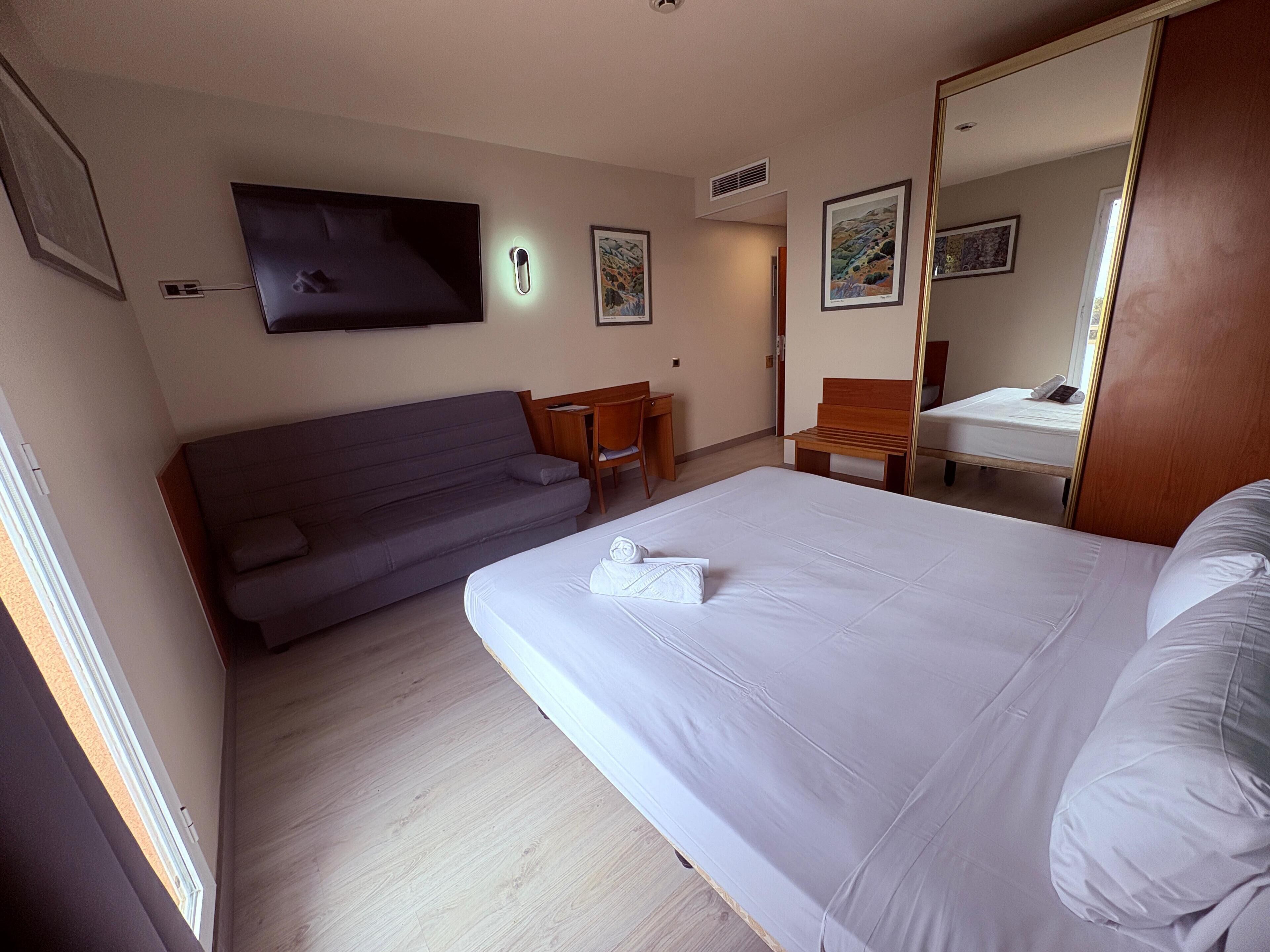 A hotel room with a bed, a sofa, a desk, and a TV.