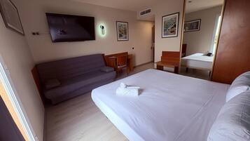 A hotel room with a bed, a sofa, a desk, and a TV.