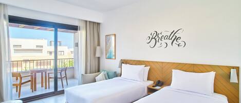 A hotel room with two beds, a balcony with a view, and a wall with the word "Breathe".