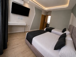 Ein modernes Hotelzimmer mit zwei Betten, einem Flachbildfernseher, einem Schreibtisch und einem Kleiderschrank.