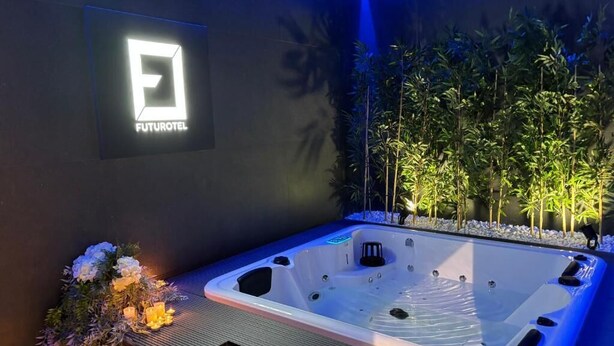 Ein modernes Hotelzimmer mit einer großen, rechteckigen Badewanne, einem Schild mit dem Hotel-Logo und einer Wandleuchte.