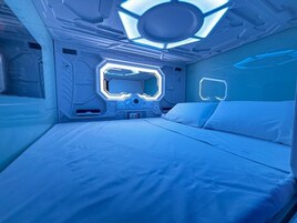 A futuristic room with a central control panel, a bed, and a circular ceiling light fixture.