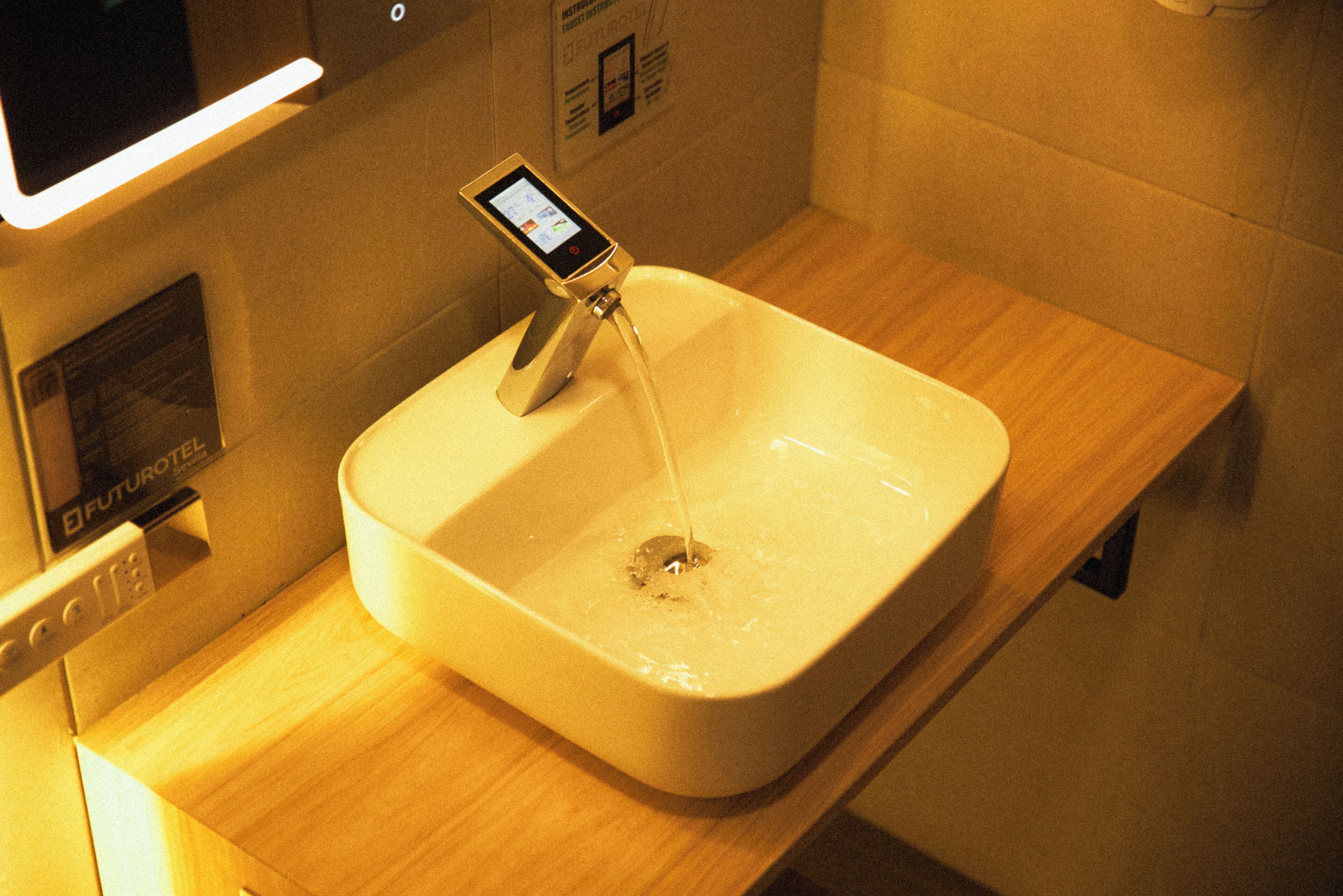 A modern bathroom with a rectangular sink, a digital faucet, and a wooden countertop.