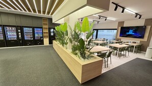 Eine moderne Hotelhalle mit Verkaufsautomaten, einem hölzernen Empfangsbereich und einem großen Bildschirm.