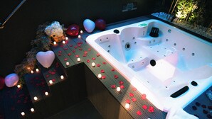 Ein Whirlpool mit Rosenblättern und Kerzen, umgeben von einer Holzterrasse.