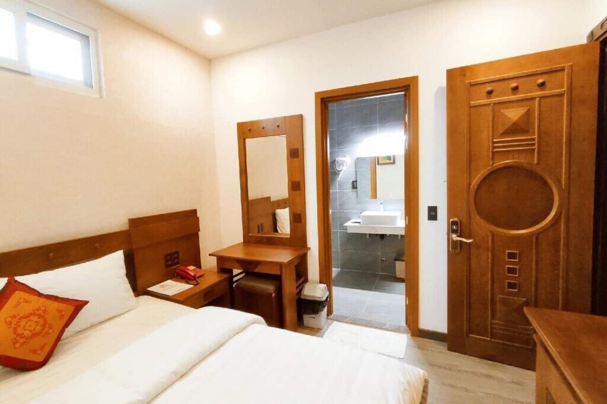 A hotel room with a bed, a desk, a chair, a mirror, and a door leading to a bathroom.