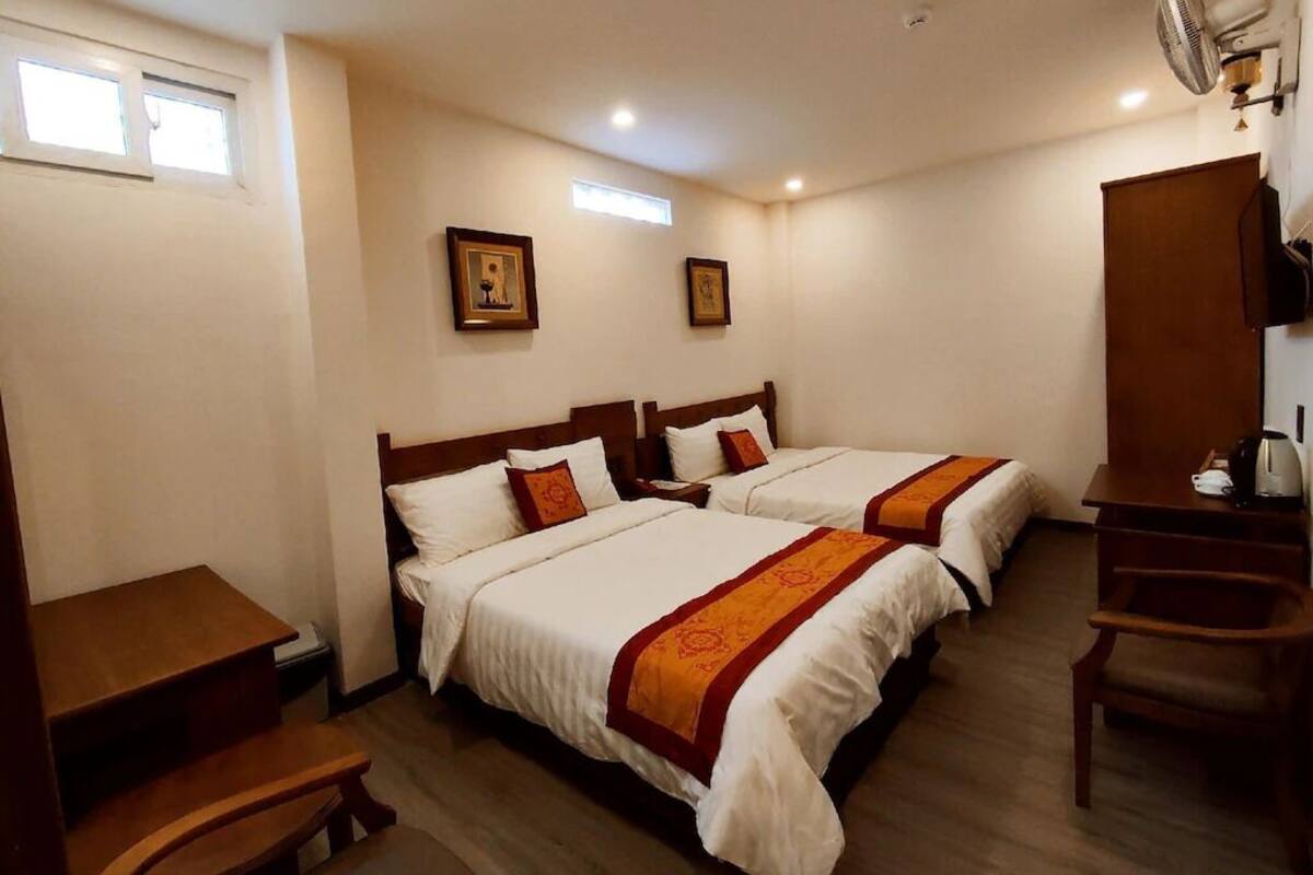 A hotel room with two beds, a desk, a chair, a small table, and a ceiling fan.