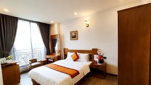 Ein Hotelzimmer mit einem großen Bett, einem Schreibtisch, einem Sessel, einem Nachttisch und einem Fenster mit Vorhängen.