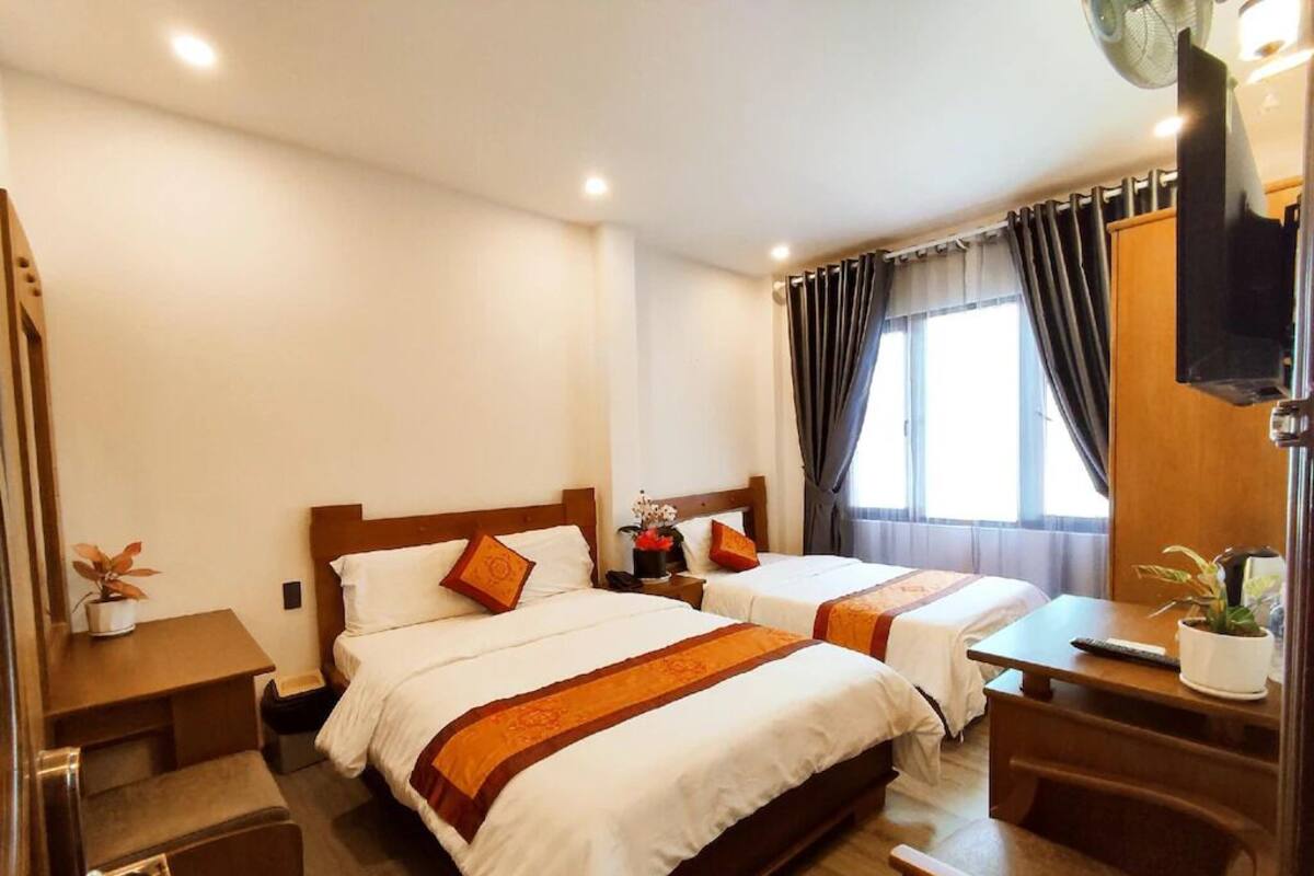 A hotel room with two beds, a desk, a chair, and a small table.