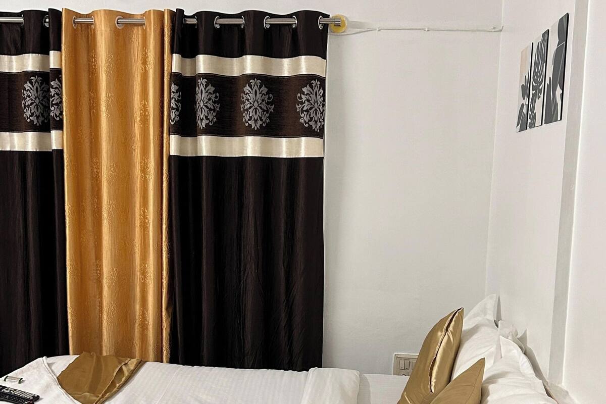 A bedroom with a bed, a wooden nightstand, a ceiling fan, and a window with black and gold curtains.