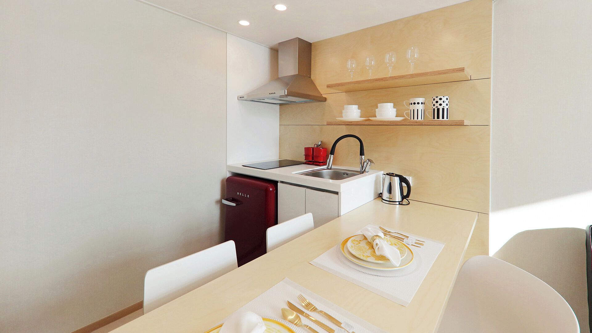 Une cuisine de taille réduite, dotée d’une cuisinière moderne, d’un évier et d’un petit réfrigérateur.